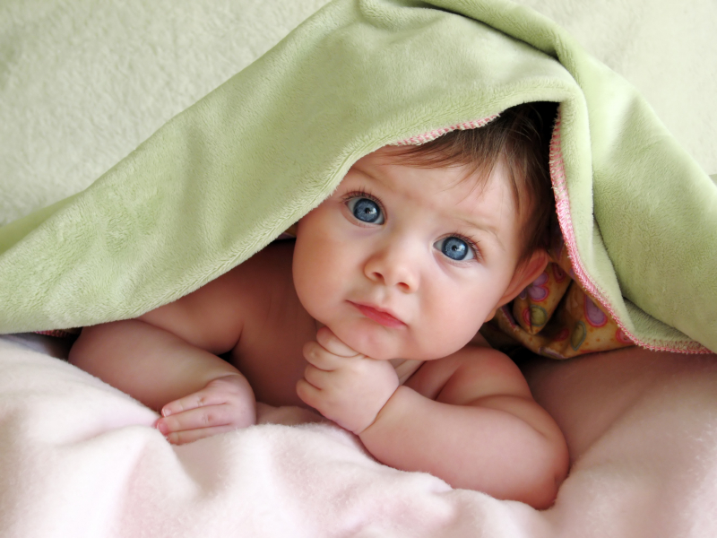 a baby playing under a green blanket